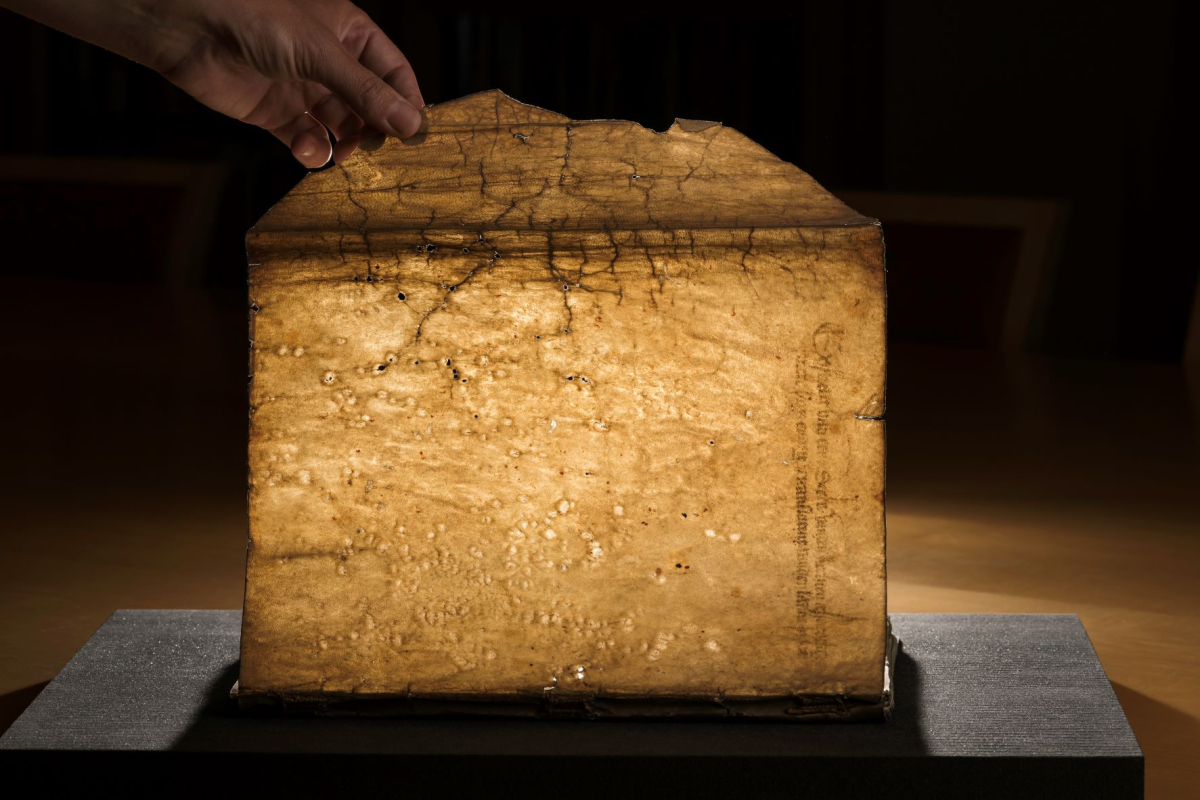 A hand holds a manuscript page upright to show its age and wear, including tiny holes.