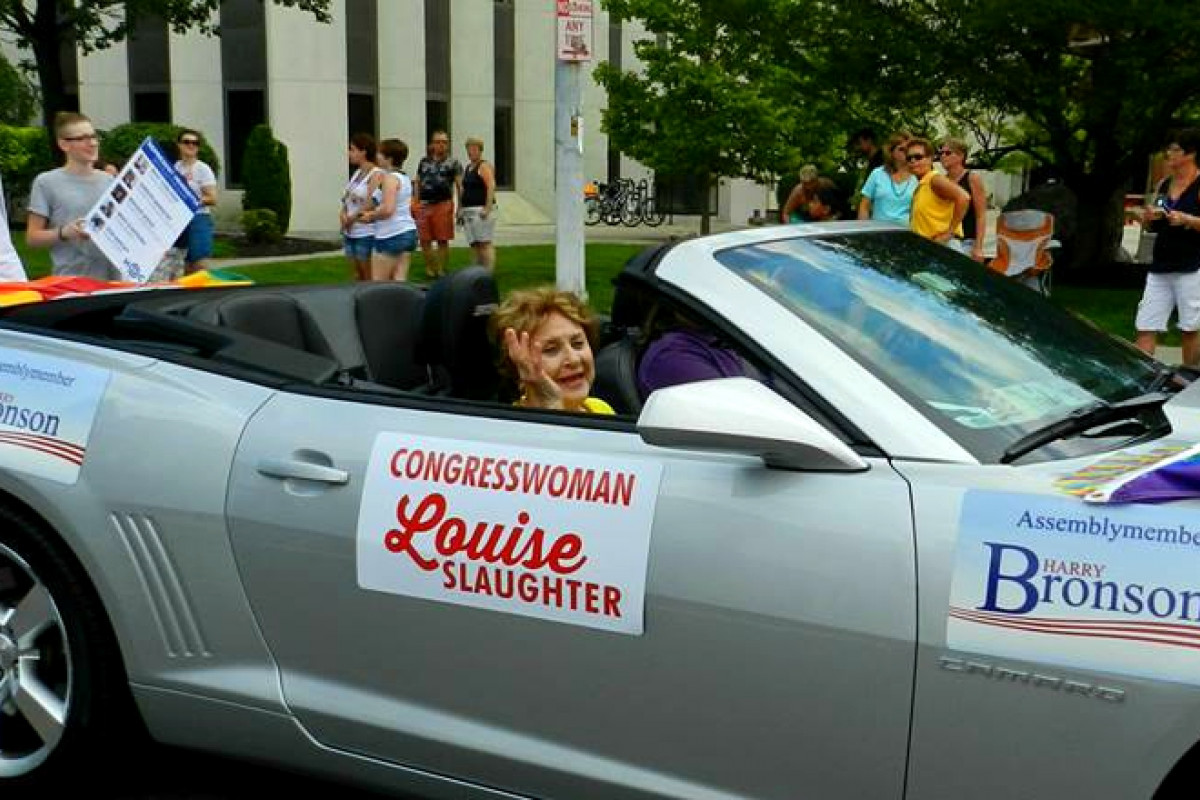 Louise Slaughter riding in a silver Camaro decorated with rainbow bunting