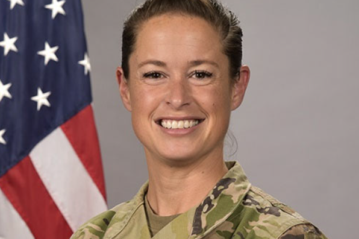 Lieutenant Cololnel Stephanie Raffo wearing military fatigues standing in front of a flag.