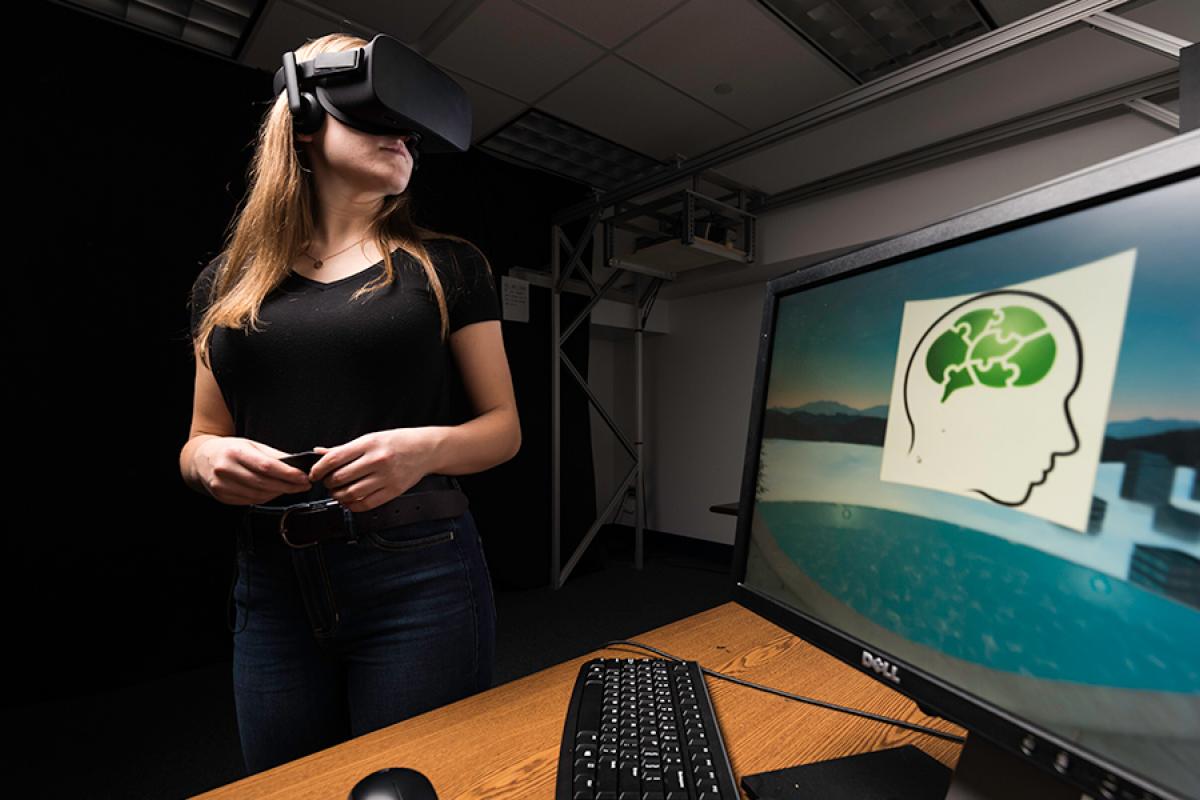 Brenna James '20 wearing a virtual reality headset with a computer in the foreground of the photo	