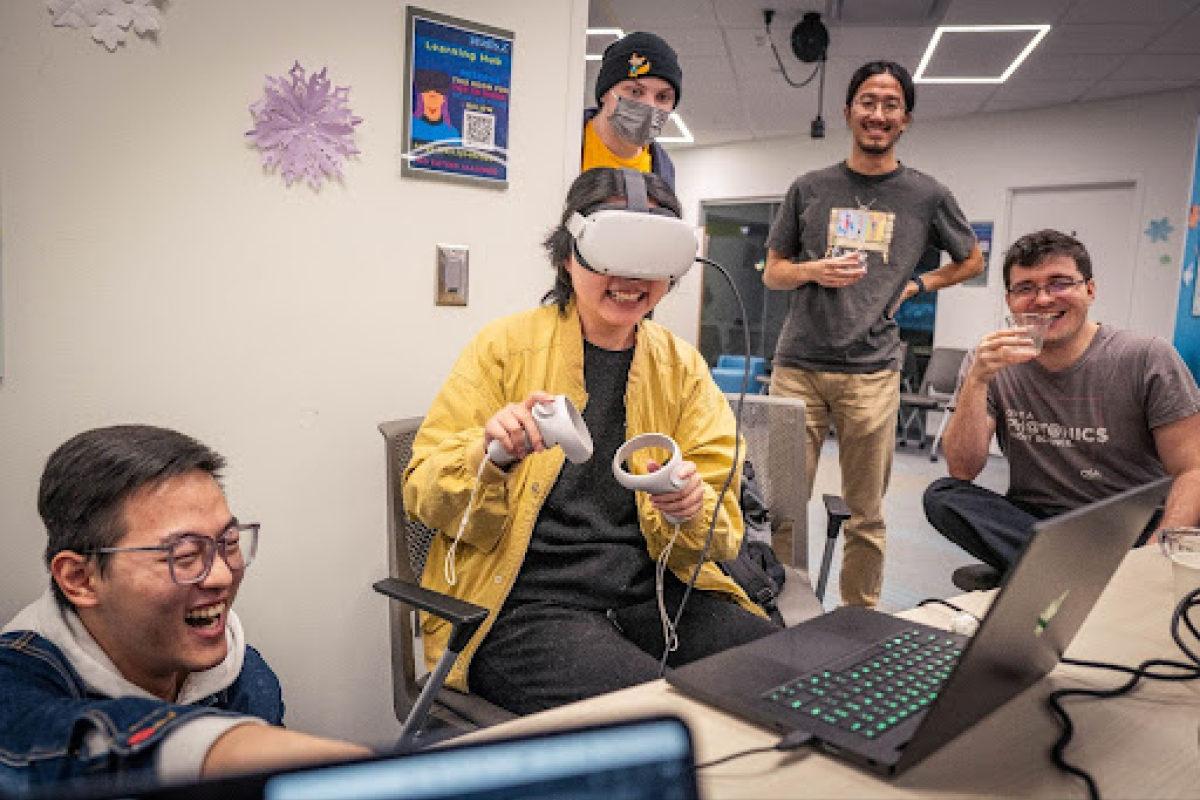 Person wearing a VR headset smiling. Others standing around them looking on. 