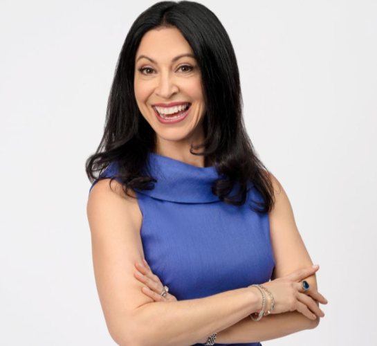 Photo of Coco Sellman, a smiling woman in a periwinkle shirt standing with her arms crossed