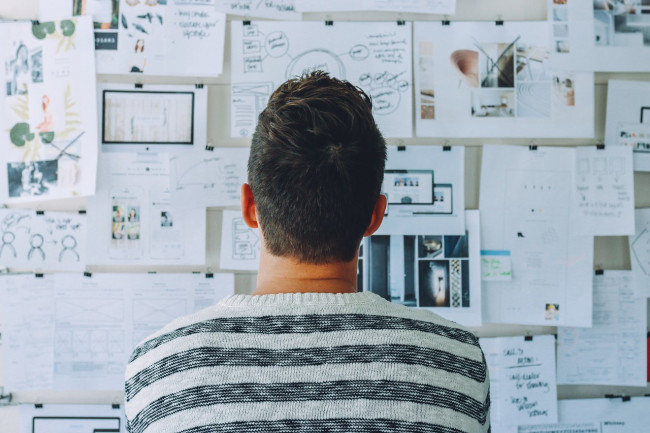 Man looking at a wall covered in pinned-up papers