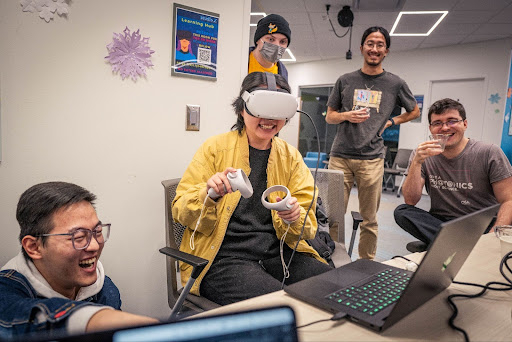 Person wearing a VR headset smiling. Others standing around them looking on. 